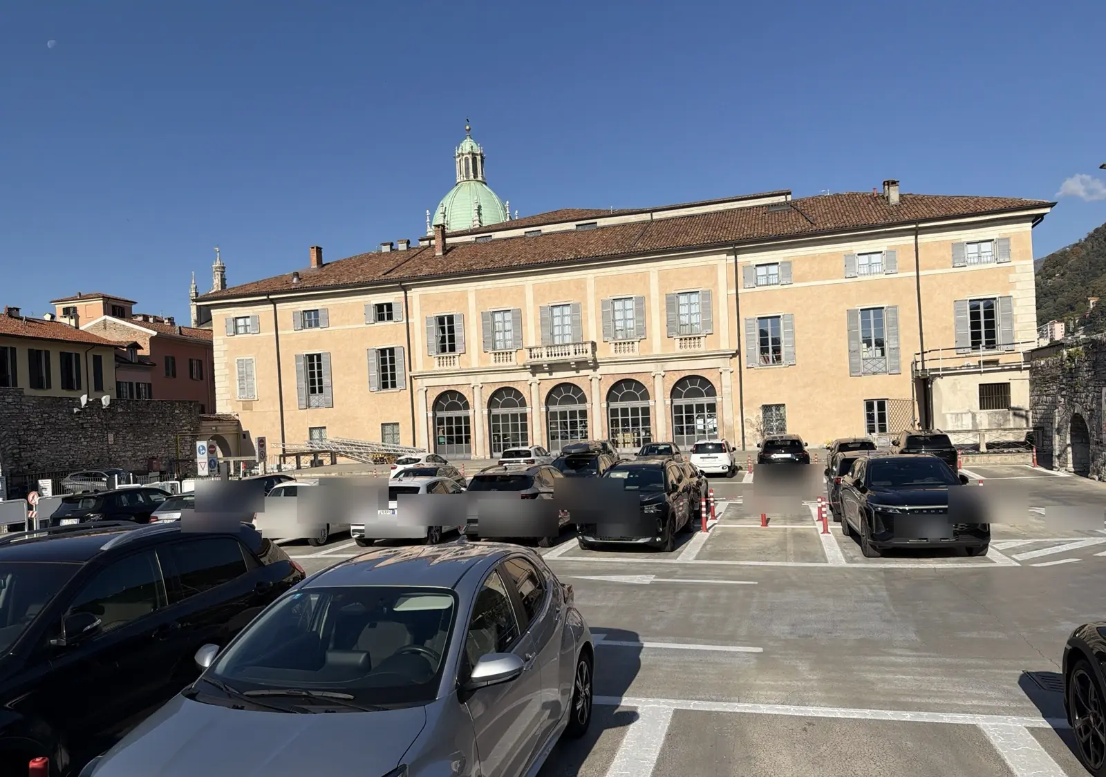 Parcheggio Arena del Teatro Sociale di Como con auto in sosta e la cupola del Duomo sullo sfondo